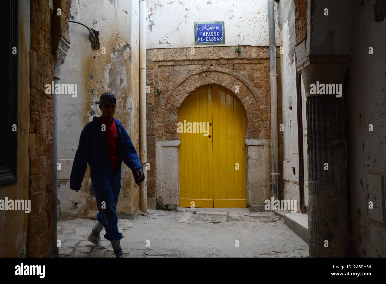 A teenage Tunisian manual labourer wearing a uniform and baseball cap walking through the pedestrian streets of the Medina of Tunis, Tunisia. Stock Photo