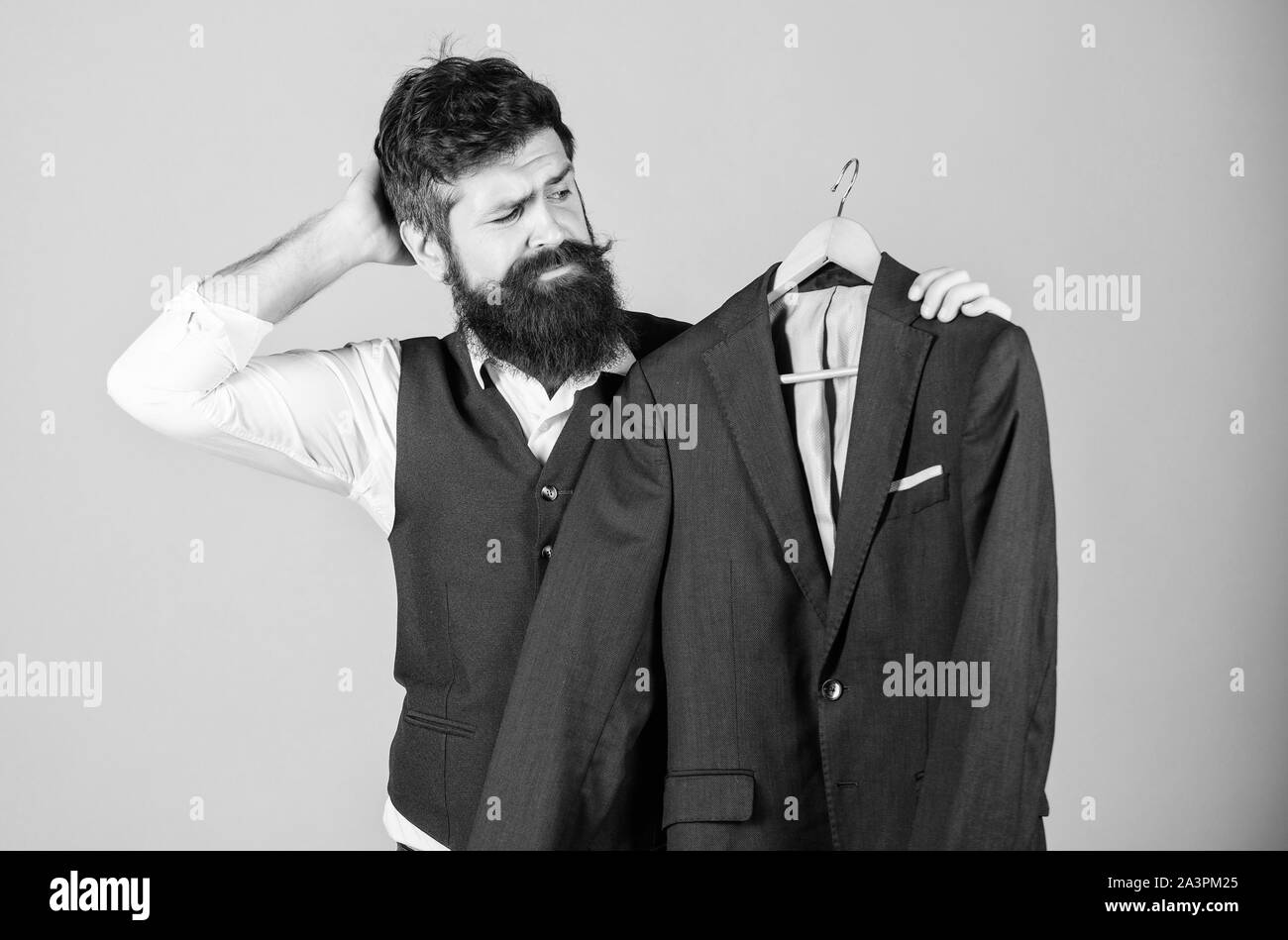 Thinking of what to wear to formal event. Hipster choosing formal suit jacket in wardrobe. Bearded man at formal wear boutique. Classy formal look of fashion model. Stock Photo