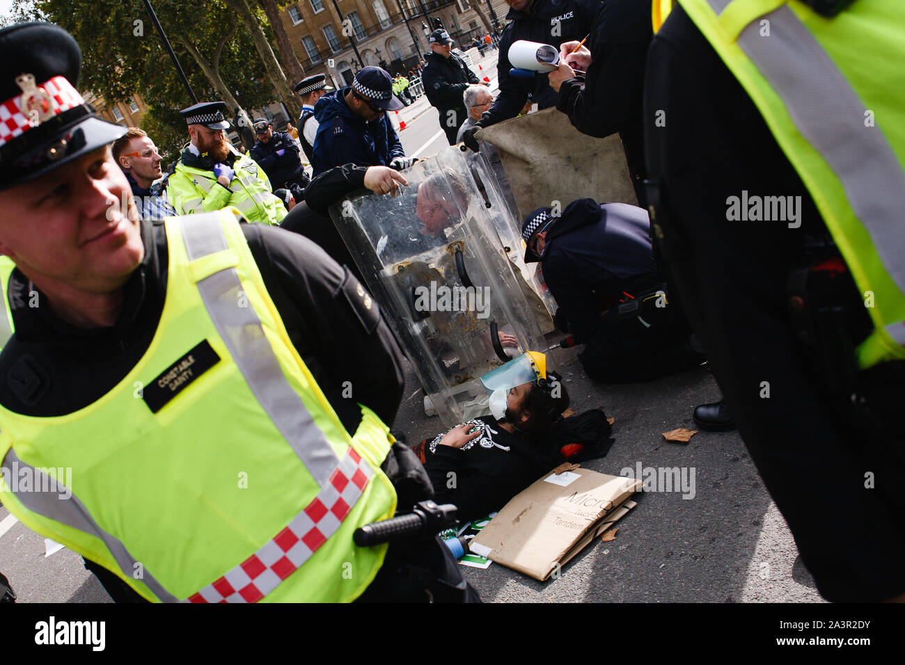 A member of climate change activist movement, Extinction Rebellion (XR) waits to be arrested on Whitehall as police officers use power tools to separate him from another demonstrator during the third day of the group's 'International Rebellion' in London.Police officers continue to clear demonstrators and tents from sites across Westminster, with activists having been warned about moving to a designated protest area around Nelson's Column in Trafalgar Square or face arrest. Similar blockades by Extinction Rebellion in April, at sites including Oxford Circus and Waterloo Bridge, saw more than 1 Stock Photo