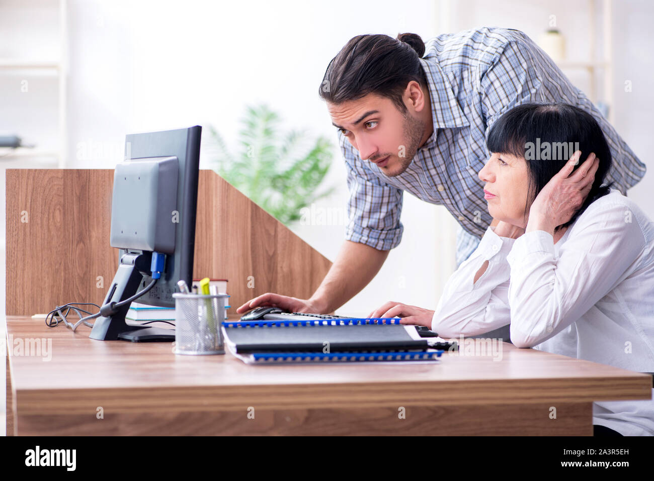 Young male employee explaining to old female colleague how to use ...