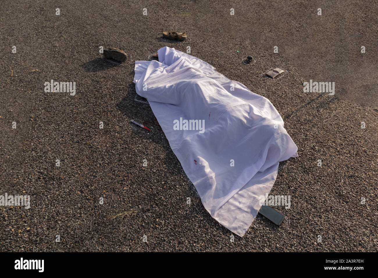 Concept of crime murder scene, High angle view of chalk outlined death body with bloody knife under white cloth on road Stock Photo