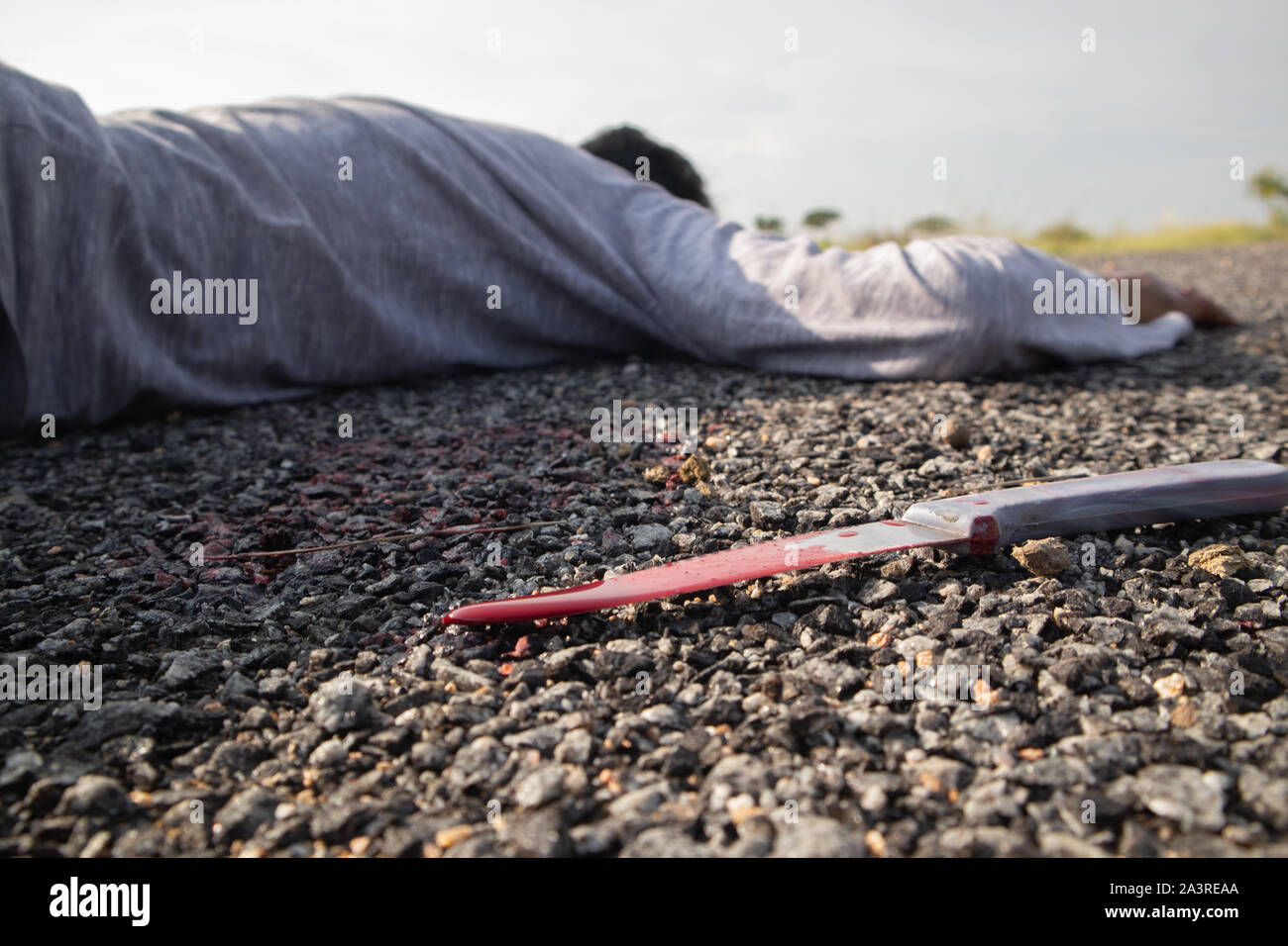 Concept of Crime murder scene, Selective focus of bloody knife on the road with dead body as background laying on Road. Stock Photo