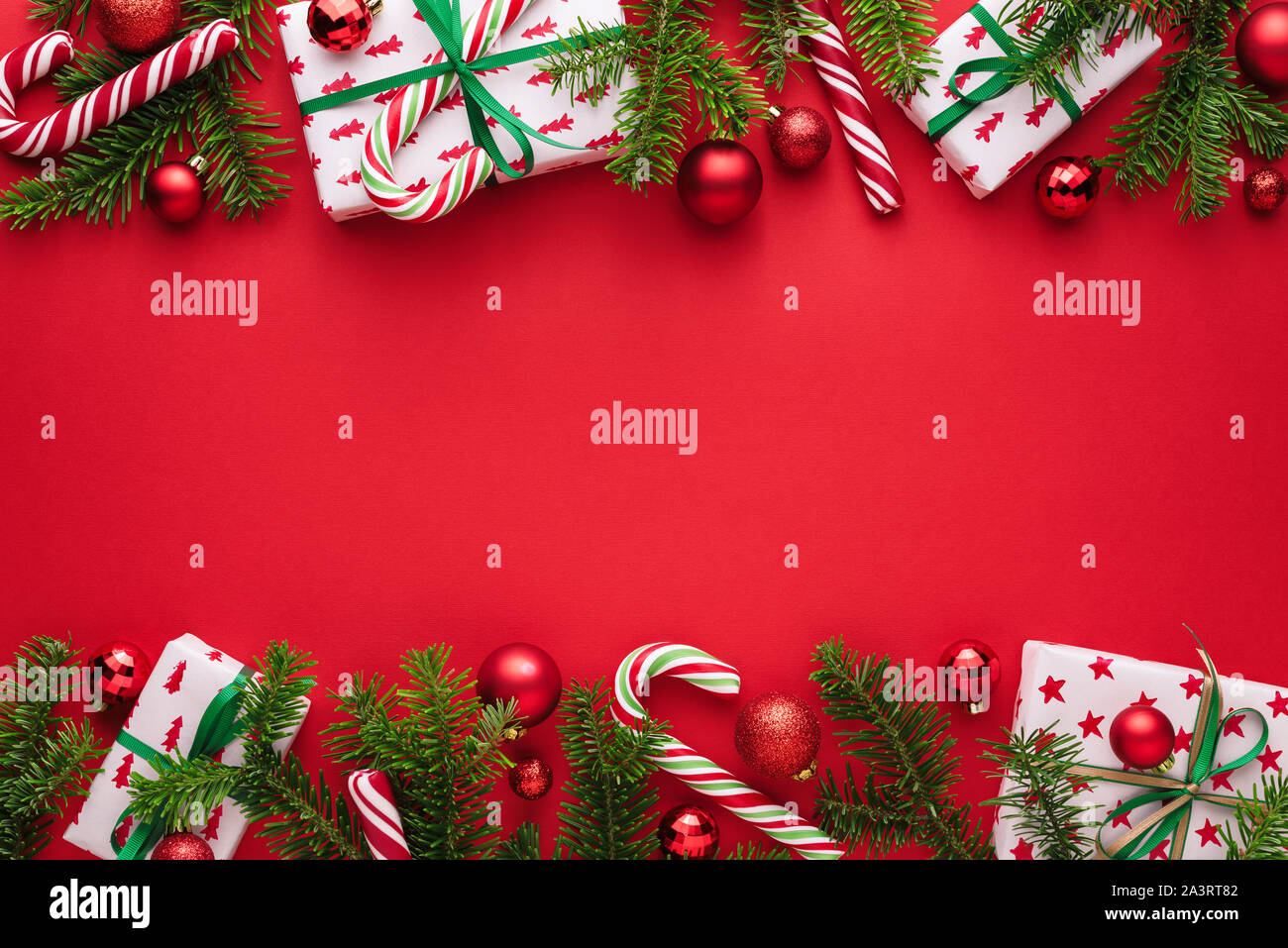 Red Christmas and New Year background. Decorative border of fir branches, gift boxes, Christmas balls and candy cane. Copy space for Christmas creep Stock Photo