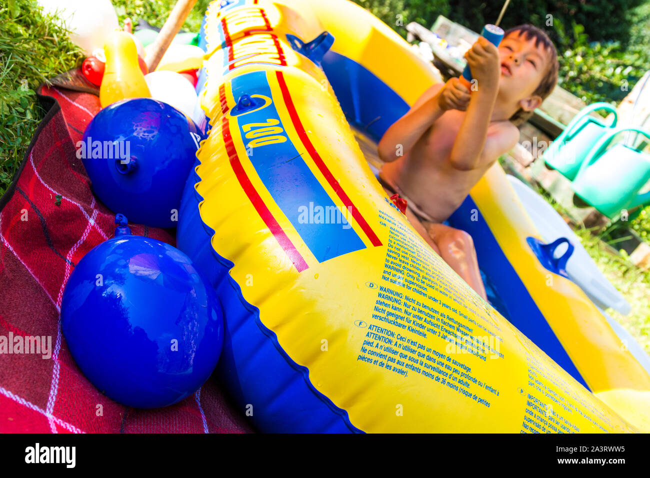 Boy child aged 5 playing with plastic toy water cannon and water bombs balloons while sitting in rubber pool in summer Stock Photo