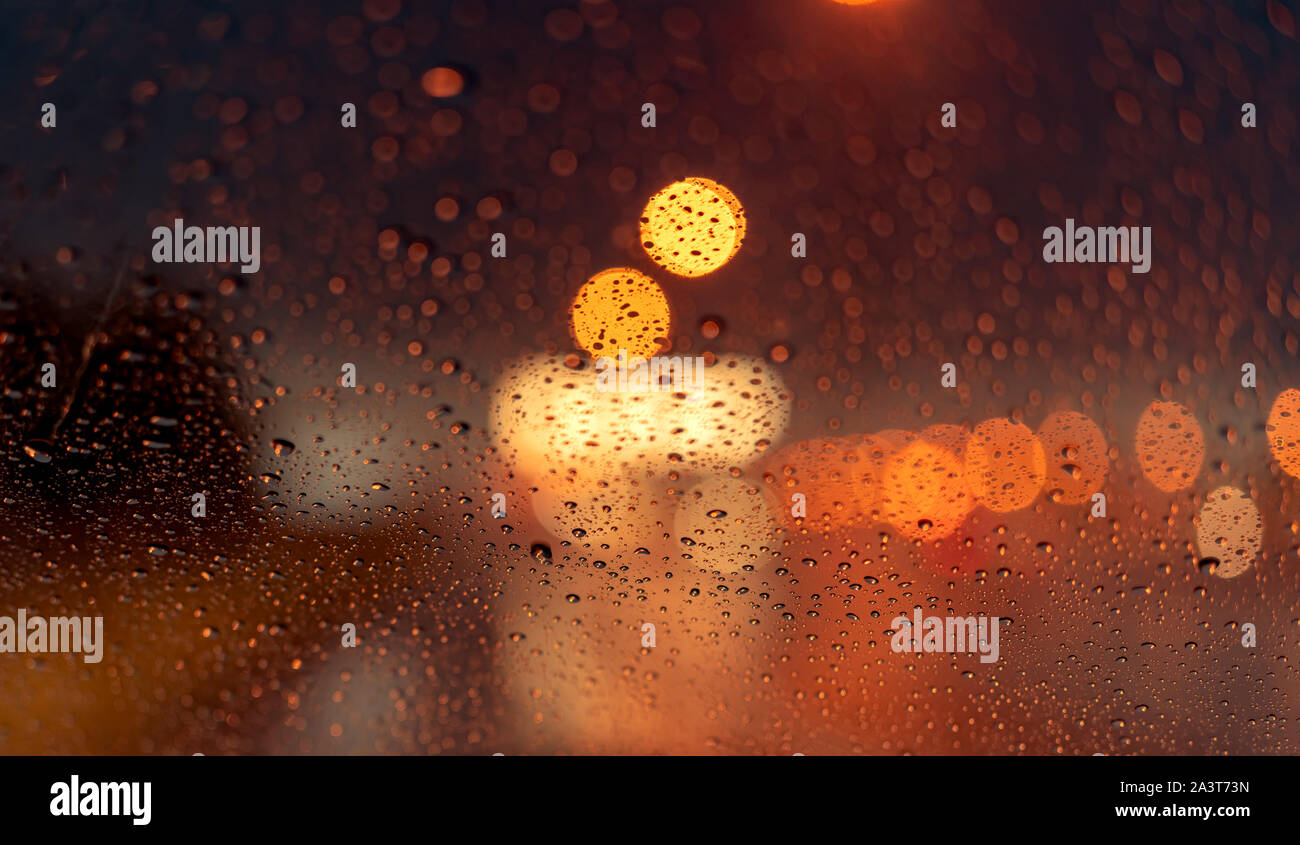 Orange night light bokeh from the street light on traffic jam day. Rainy day. transparent glass window with a raindrop. Romantic weather. City life. Blur Stock Photo