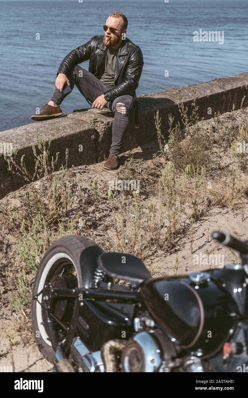 Attarctive bearded man sitting by the roadside enjoying the view of the ocean Stock Photo