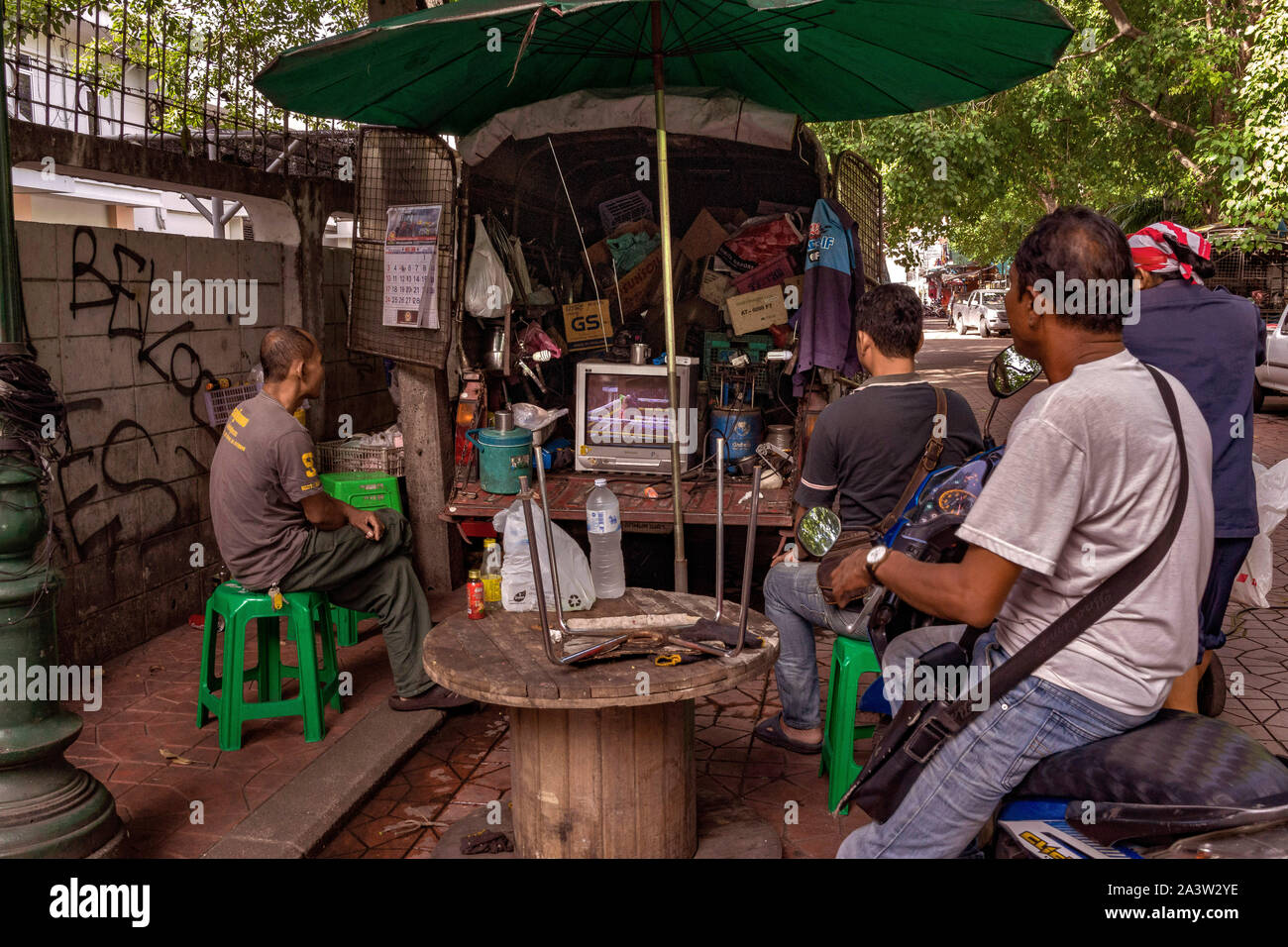 Locals gather in the street around and old CRT TV to watch the big Muay Thai Kickboxing Fight in Bangkok Thailand. Will the Local Champ win? Stock Photo