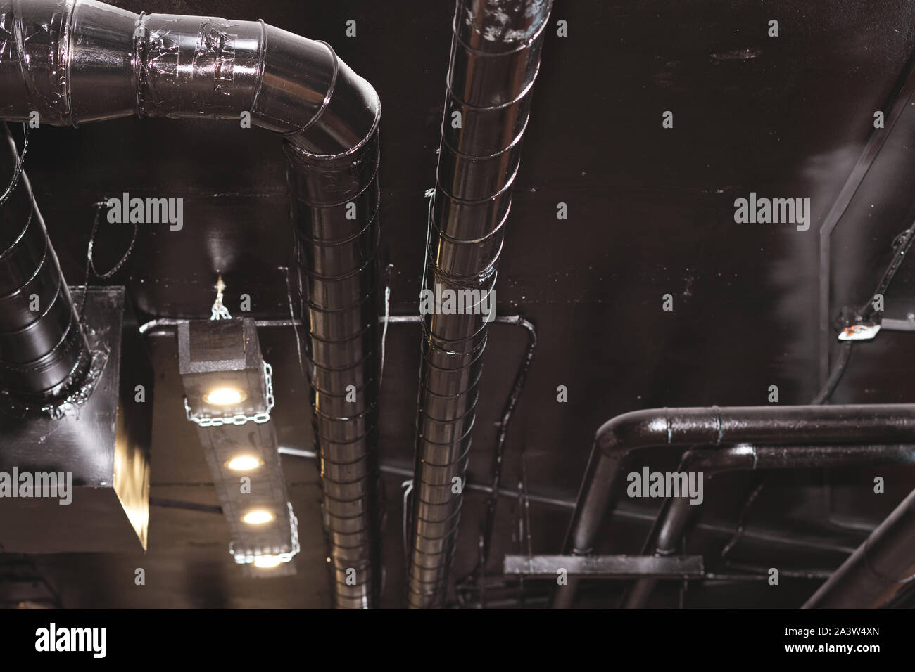 Metal pipes under the ceiling. Pipes are black. Spot lights on metal chains. Brutal interior. The solution is under repair. Basement Stock Photo