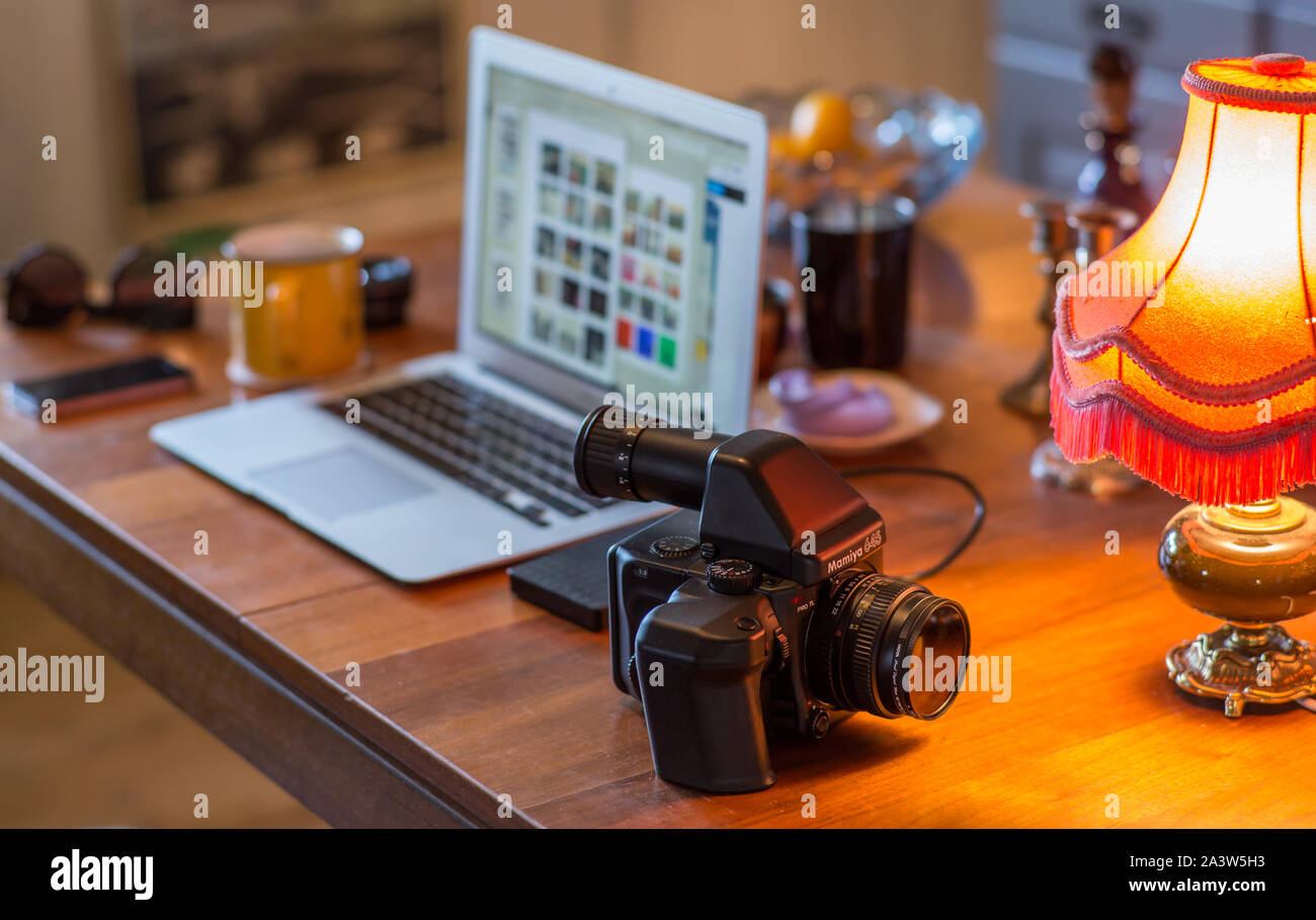 A view of a home office with a medium format analog camera on a table in front of a laptop and other various objects. Stock Photo