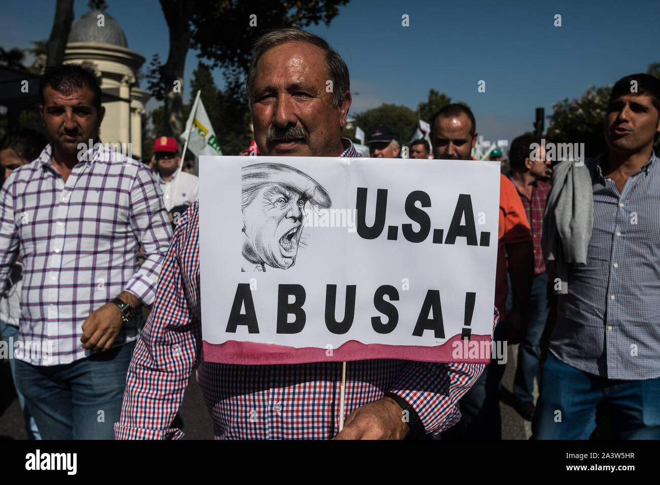 Madrid, Spain. 10th October, 2019. A man carrying a placard that reads 'USA abuses' with the face of Donald Trump during a demonstration. Olive oil producers march to the Agriculture Ministry to denounce low prices of olive oil and against the 25 percent tariff that Spanish olives and olive oil will face in the United States. Credit: Marcos del Mazo/Alamy Live News Stock Photo