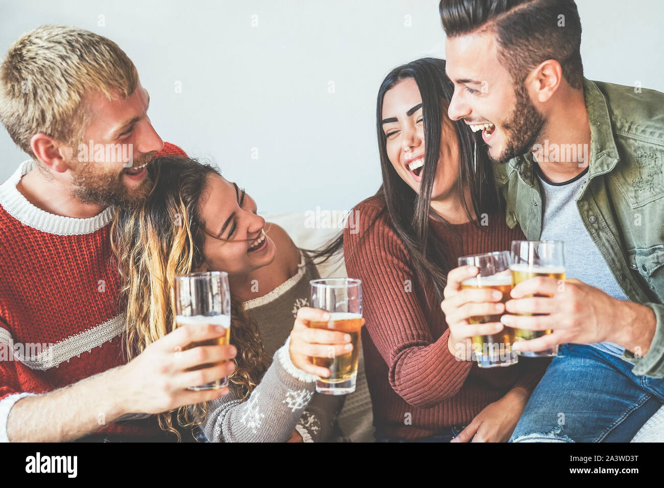 Group of happy friends cheering with beer at home - Millennial Young people having fun drinking and laughing together sitting on sofa Stock Photo