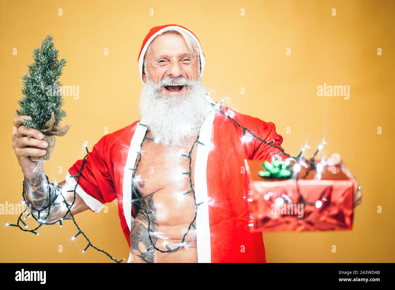 Happy tattoo hipster santa claus equiped with white lights giving christmas gifts - Trendy beard senior wearing xmas clothes and holding presents Stock Photo