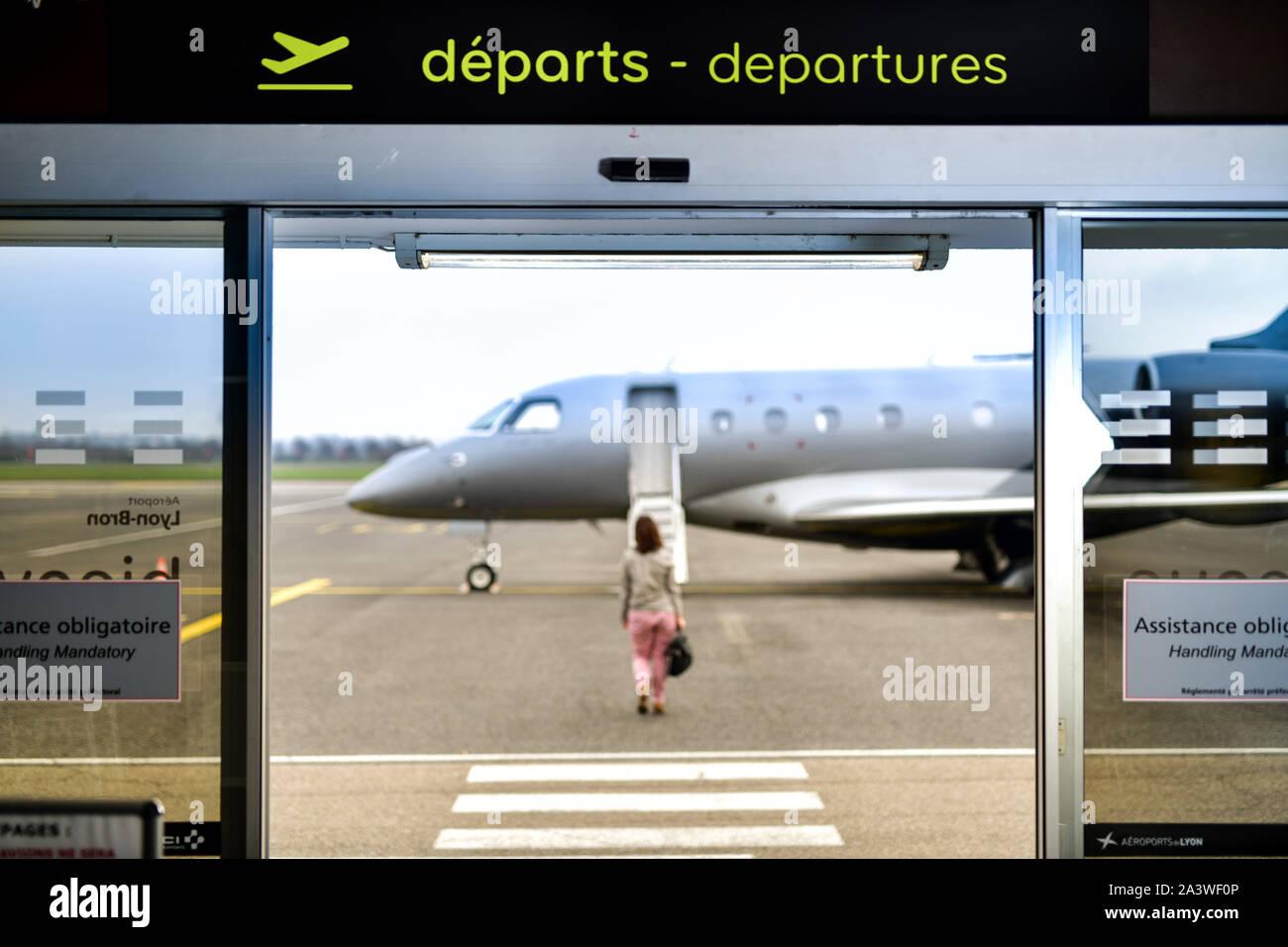 Lyon-Bron Airport, France's third largest business airport. Woman, passenger with luggage passing through the departure gate to reach a jet parked on Stock Photo