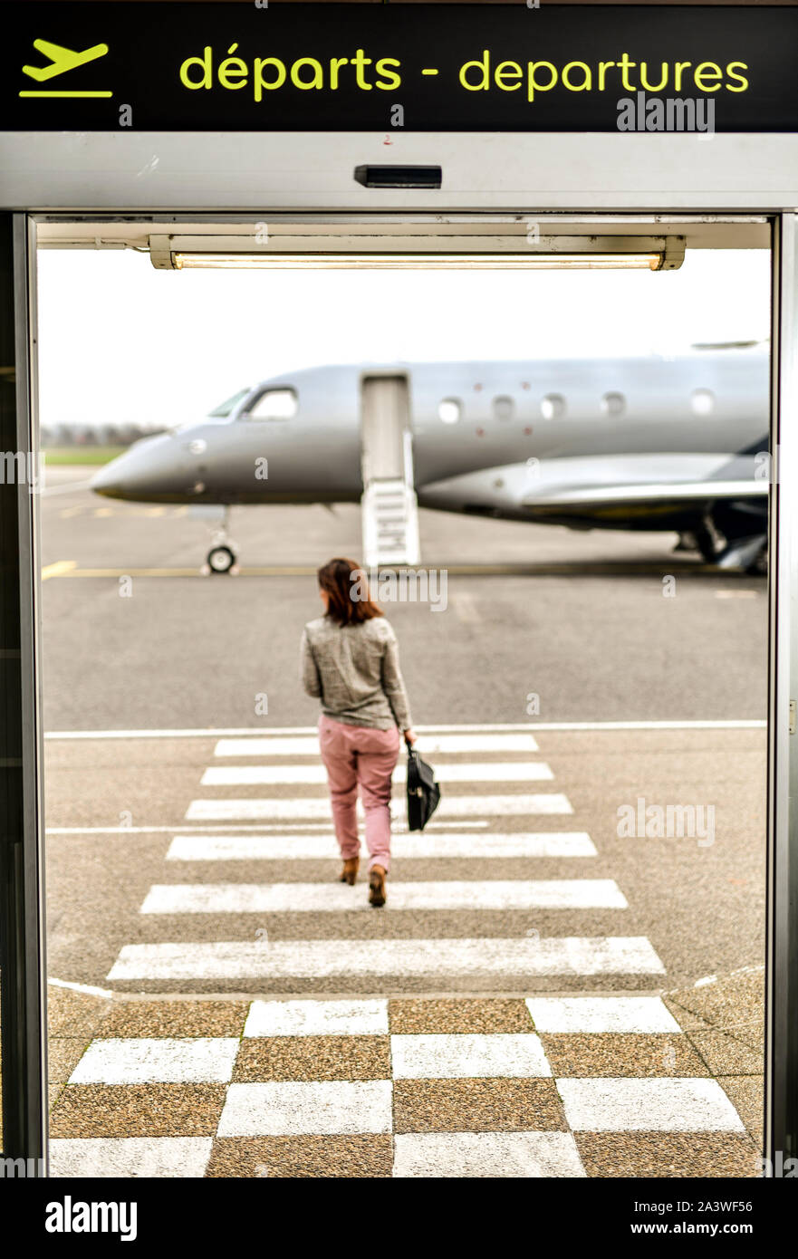 Lyon-Bron Airport, France's third largest business airport. Woman, passenger with luggage passing through the departure gate to reach a jet parked on Stock Photo