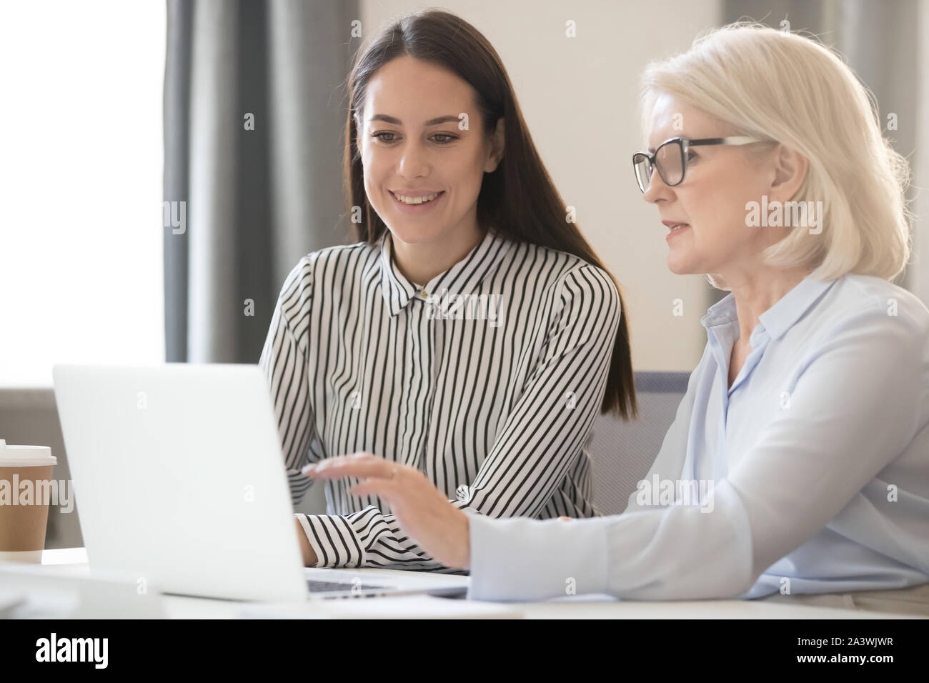 Confident experienced female employees share information with young worker Stock Photo