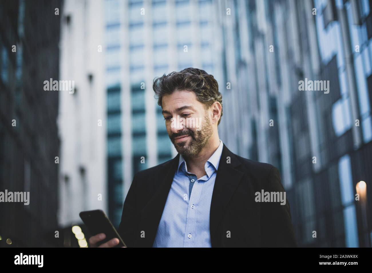 Businessman walking in city using smartphone Stock Photo
