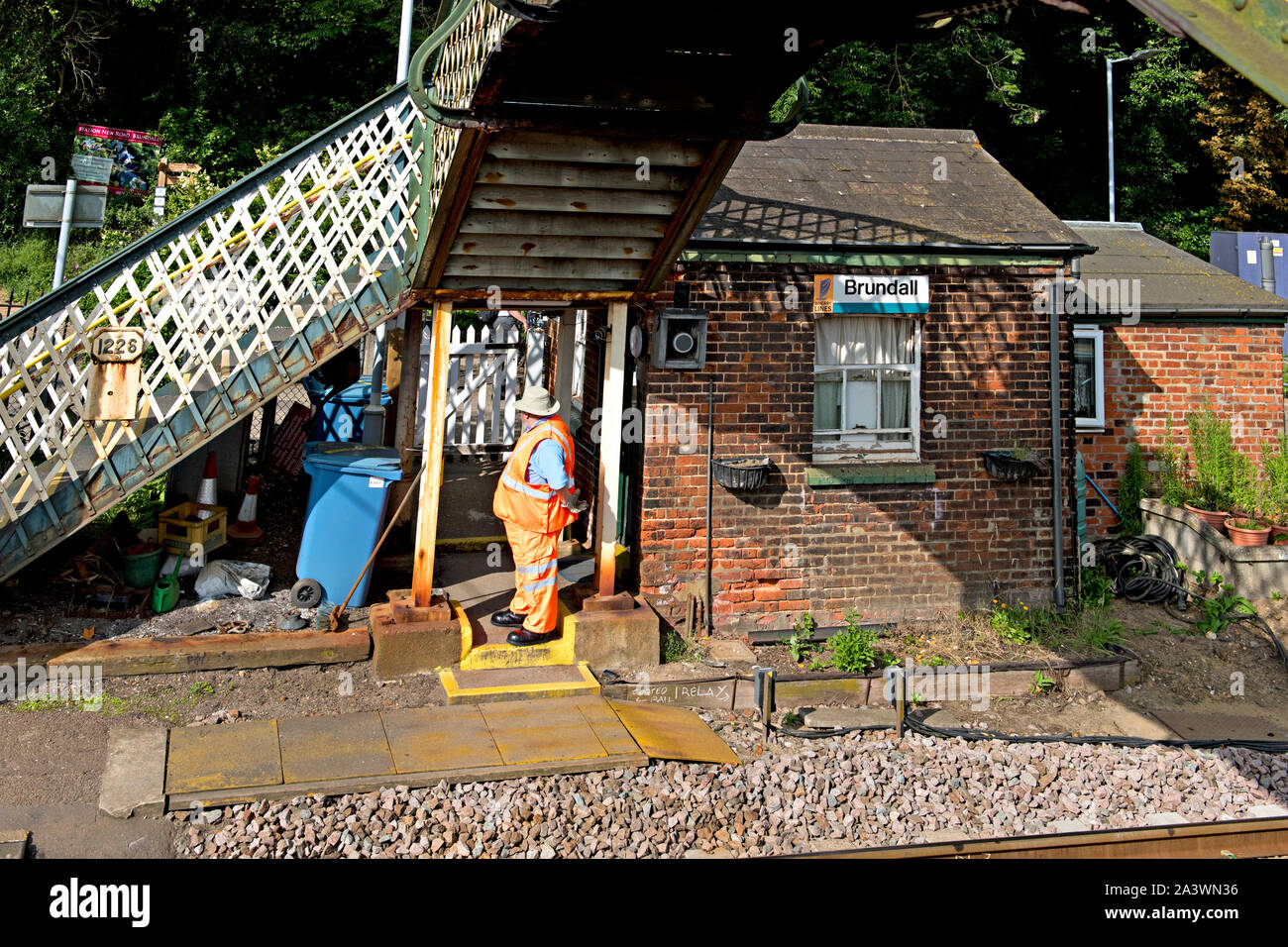 The crossing keeper at Brundall railway station between Lowestoft and Norwich awaits his next duty. He stands beside a brick built keeper's hut Stock Photo