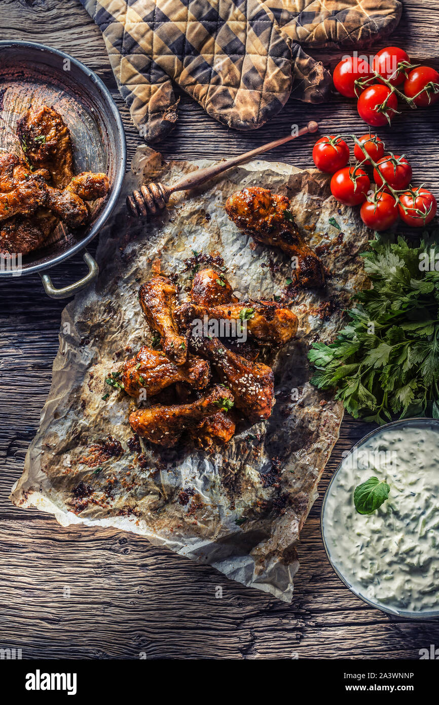 Roasted chicken legs barbecue on baked paper with tzatziki sauce tomatoes and parsley herbs. Stock Photo