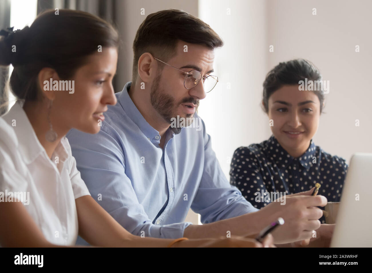 Serious caucasian teacher instructing diverse students explaining computer project Stock Photo