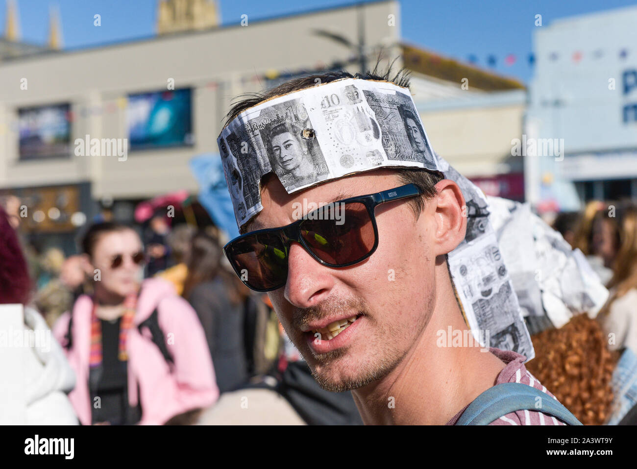 A young person wearing a hat made of photocopied Ten Poiund notes participating in the Extinction Rebellion climate strike in Truro City City in Cornw Stock Photo