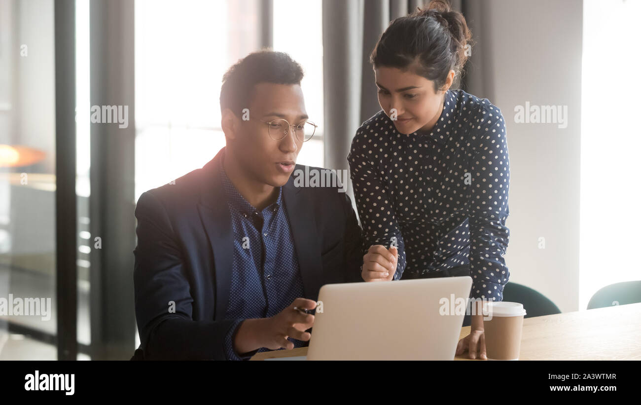 Indian mentor coworker talk help black intern explain computer work Stock Photo