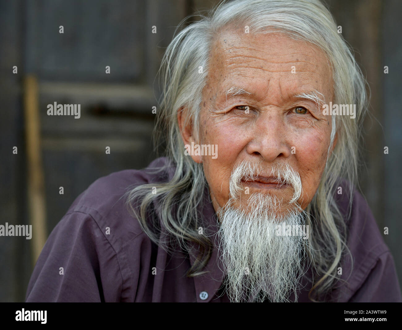 Elderly Sino-Burmese man with long grey hair and a traditional long Chinese beard poses for the camera. Stock Photo