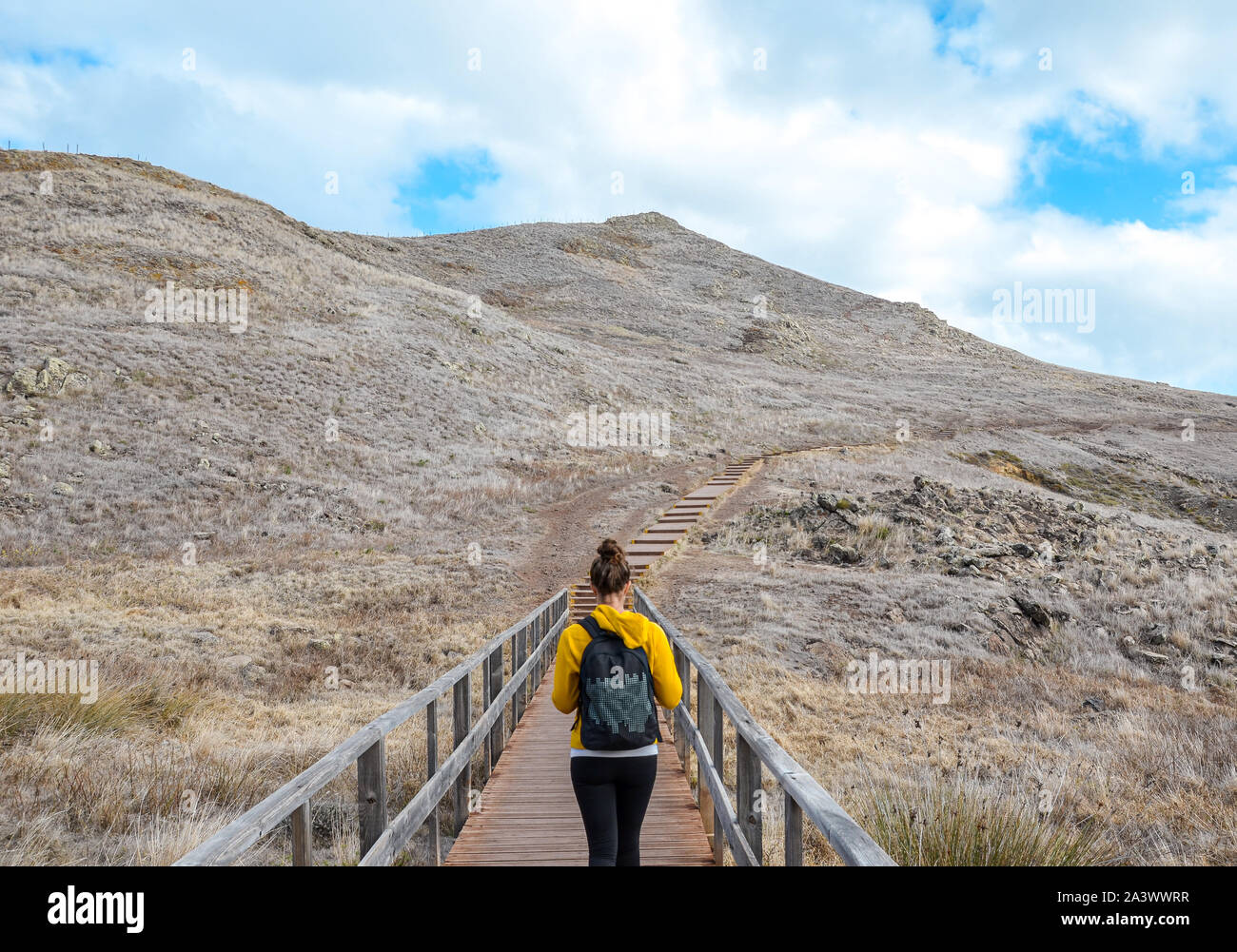 Young girl in yellow sweater on hiking path in Ponta de Sao Lourenco in Madeira, Portugal. Peninsula in eastern part of the island. Volcanic landscape. Woman traveller. Adventure concept. Stock Photo