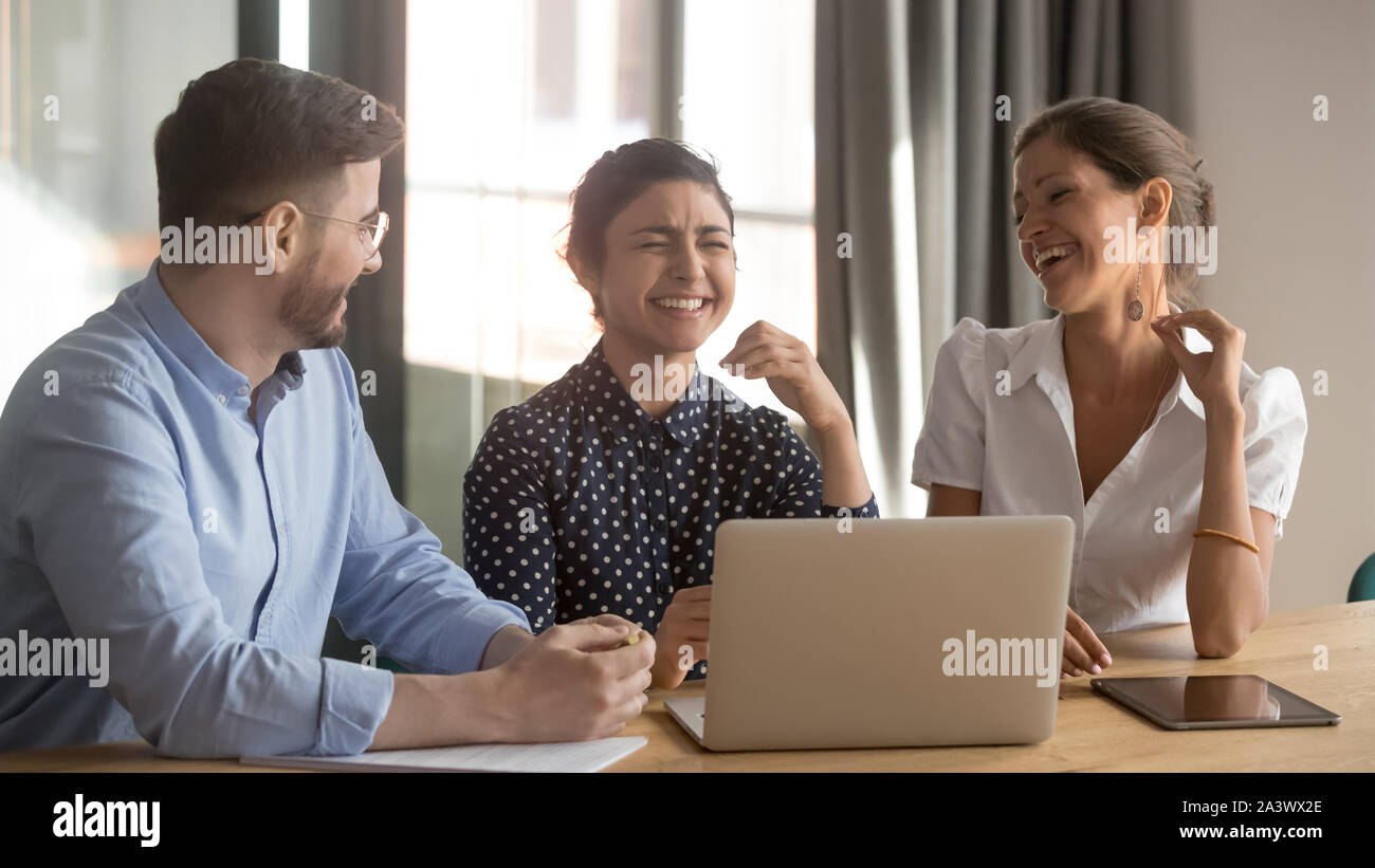 Three happy diverse coworkers talking laughing working together with laptop Stock Photo
