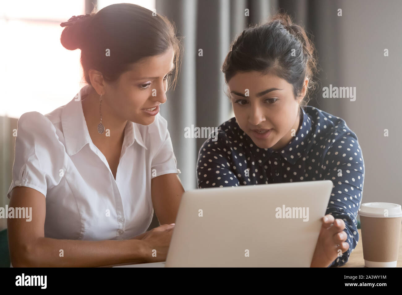 Focused diverse ethnicity female coworkers team brainstorming pointing on laptop Stock Photo