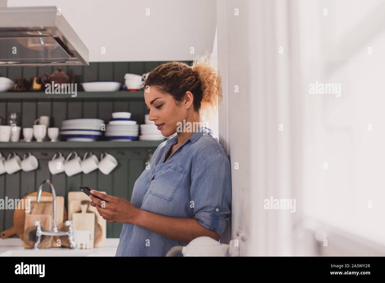 Adult female looking at smartphone in kitchen Stock Photo
