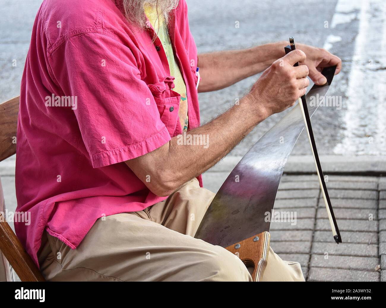 old man playing music on a singing saw on the street Stock Photo