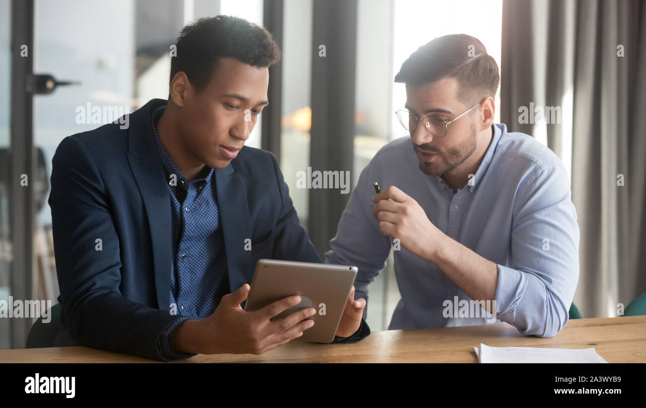 Focused black and white partners discussing project using digital tablet Stock Photo