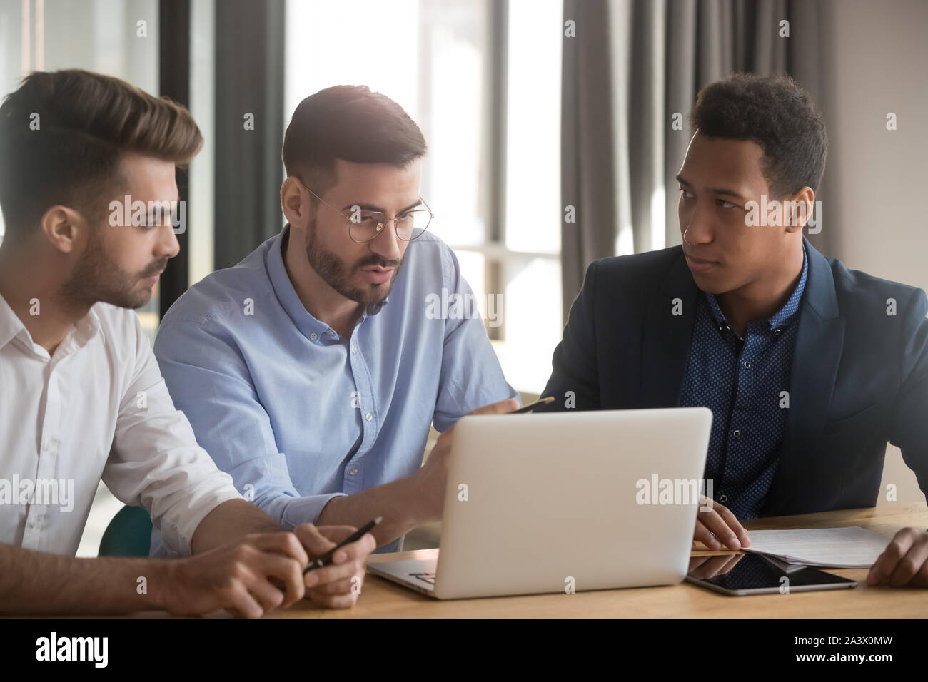 Serious mentor and diverse businessmen discuss online project at meeting Stock Photo
