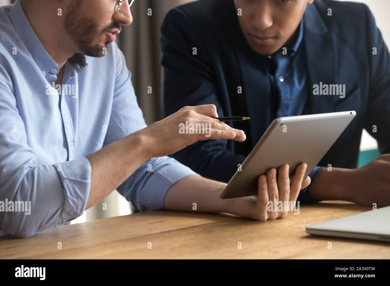 Diverse businessmen talking using digital tablet sit at desk, closeup Stock Photo