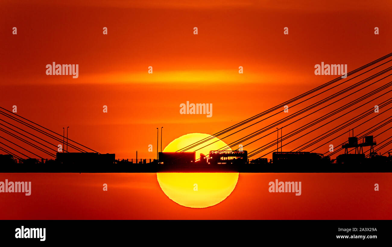 Sunset over the cable-stayed bridge with silhouette of car crossing the sea bay Stock Photo