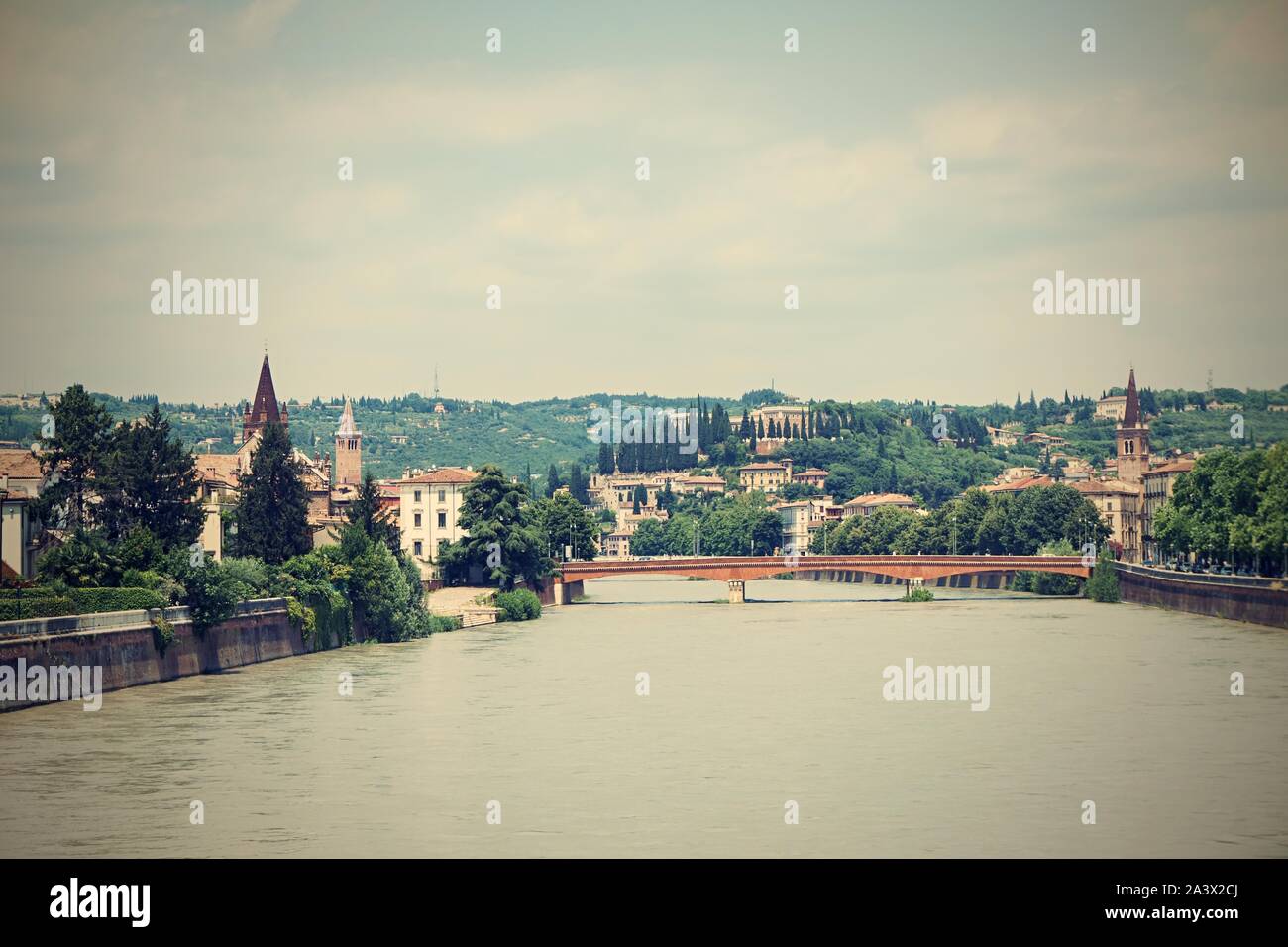 Horizontal photo with view on Adige river. River flows through famous Verona city in Italy. Old bridge and several buildings are visible in background Stock Photo