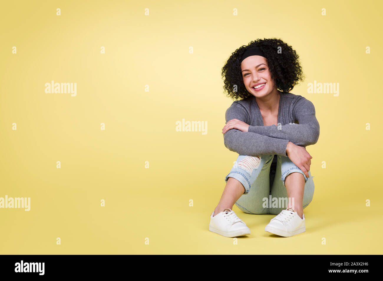 Happy girl sitting smiling on yellow background with copy space. Stock Photo