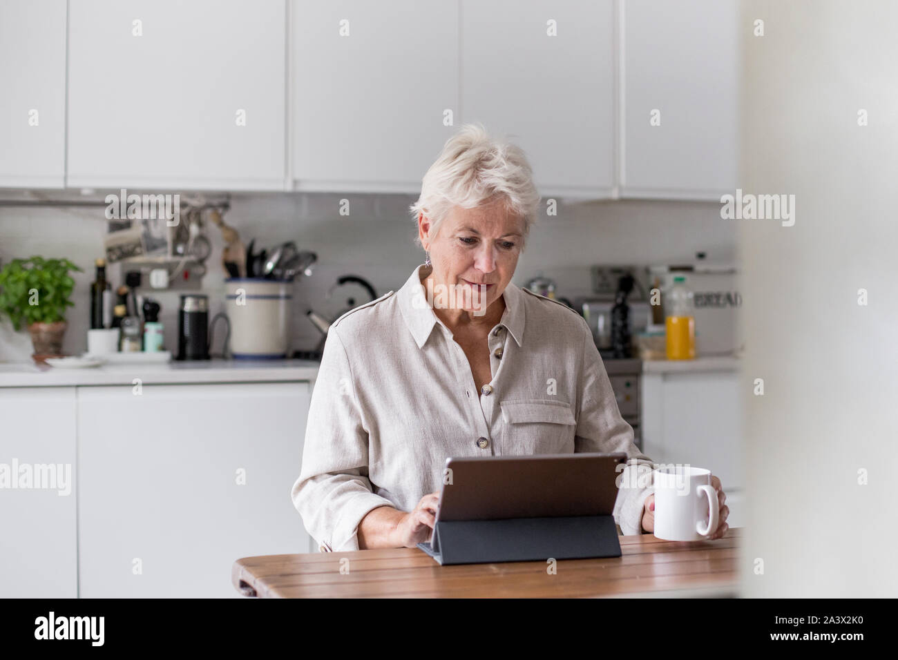 Mature adult woman in kitchen using a digital tablet with keypad Stock Photo