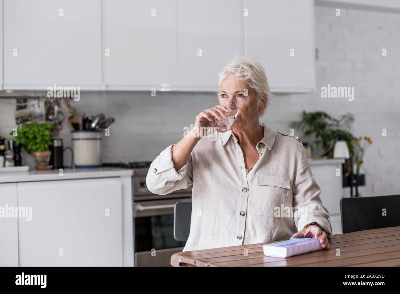 Mature adult woman taking medicine at home in the kitchen Stock Photo