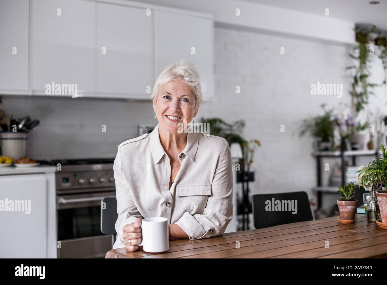 Portrait mature adult woman looking out of window with a mug of tea Stock Photo