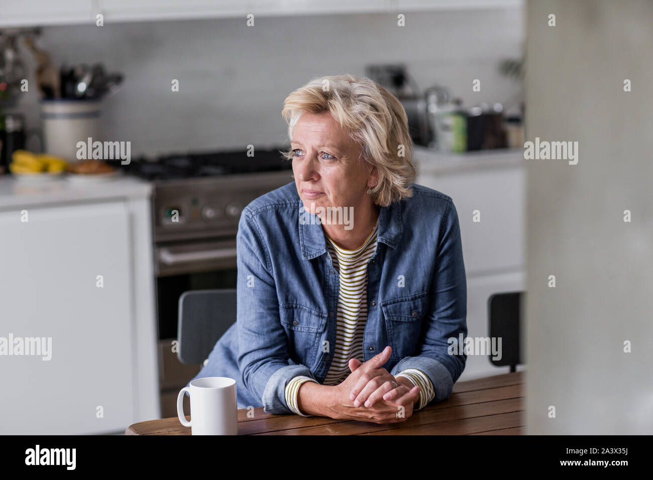 Mature adult woman looking out of window with a mug of tea Stock Photo