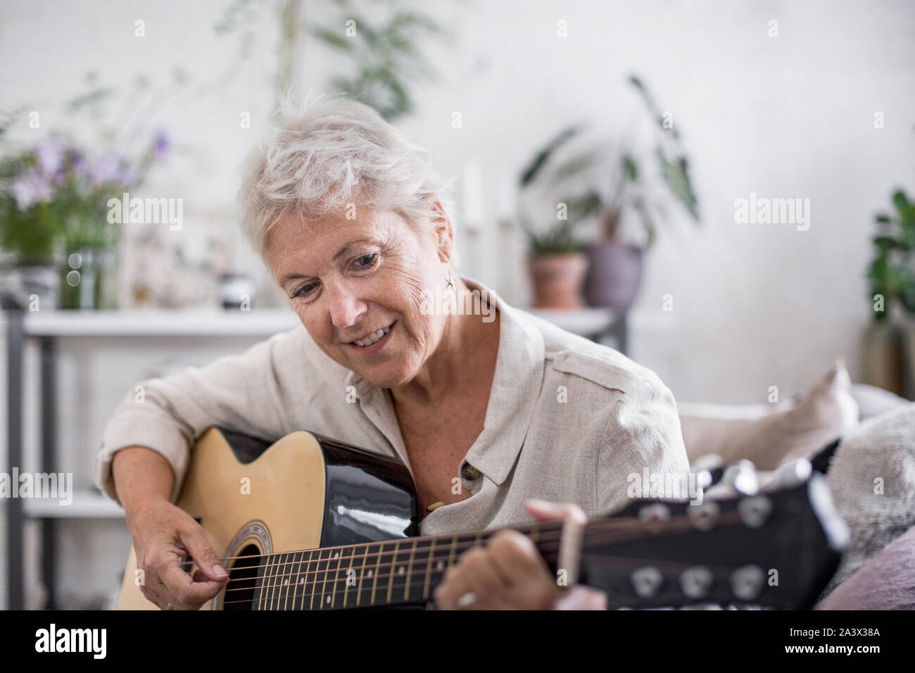 Mature adult female learning to play the guitar at home Stock Photo