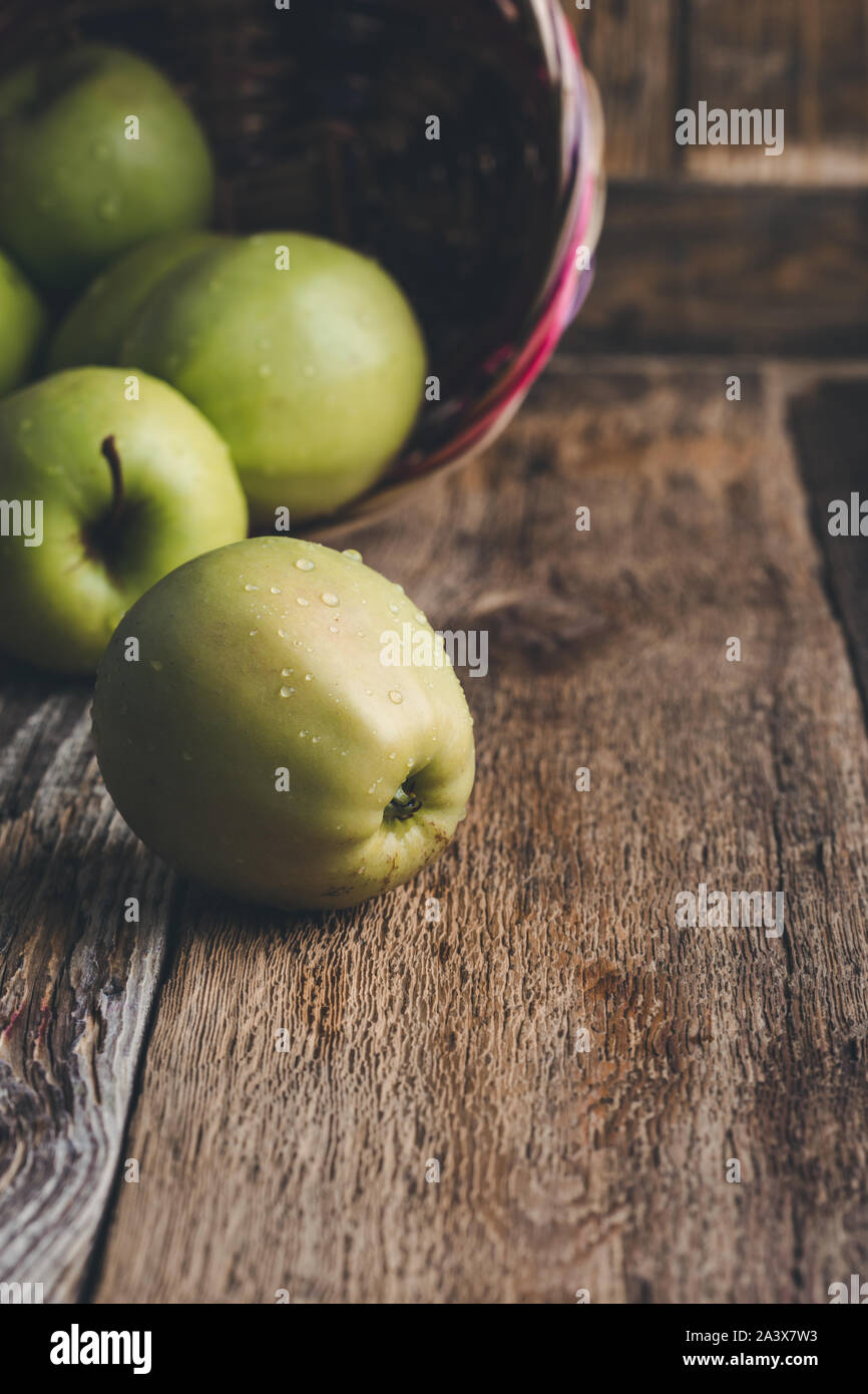 Close-up of fresh ripe  green apples In wicker  basket on rustic wooden table at home, plant based food Stock Photo