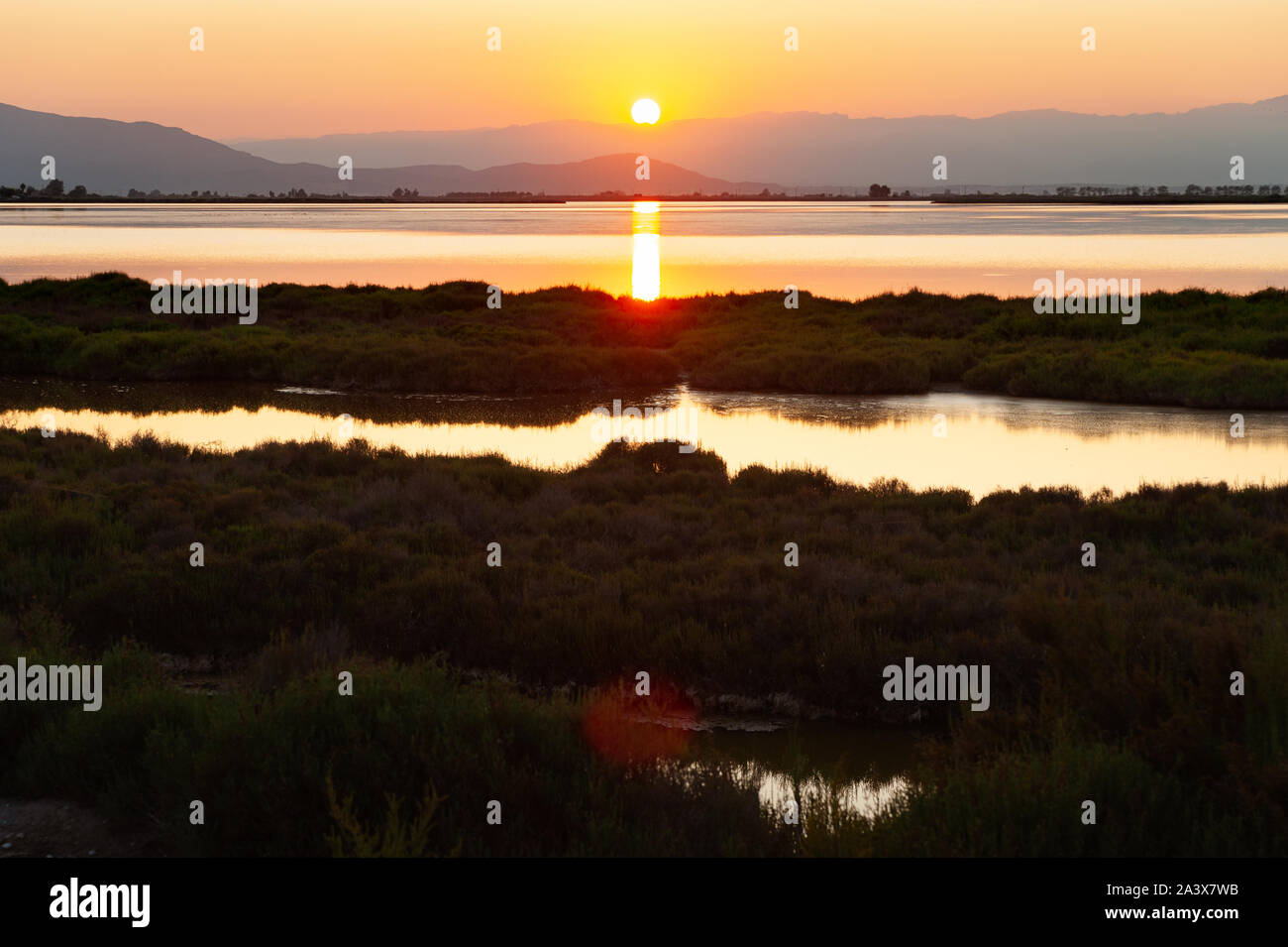 sun setting behind mountains and reflecting in ebro river and sea in ebro delta national park in catalunya, spain, with warm colors Stock Photo