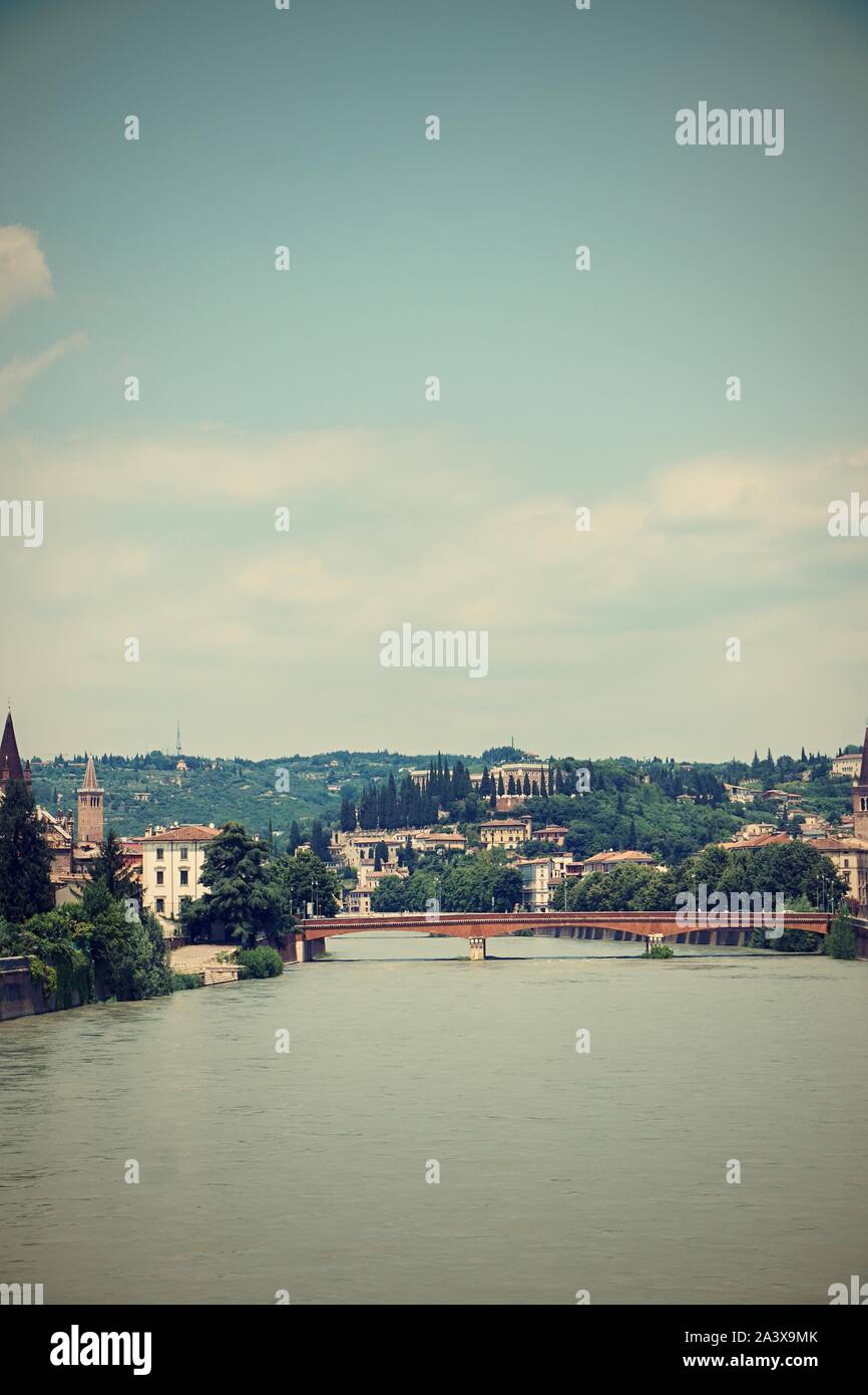 Vertical photo with view on Adige river. River flows through famous Verona city in Italy. Old bridge and several buildings are visible in background. Stock Photo