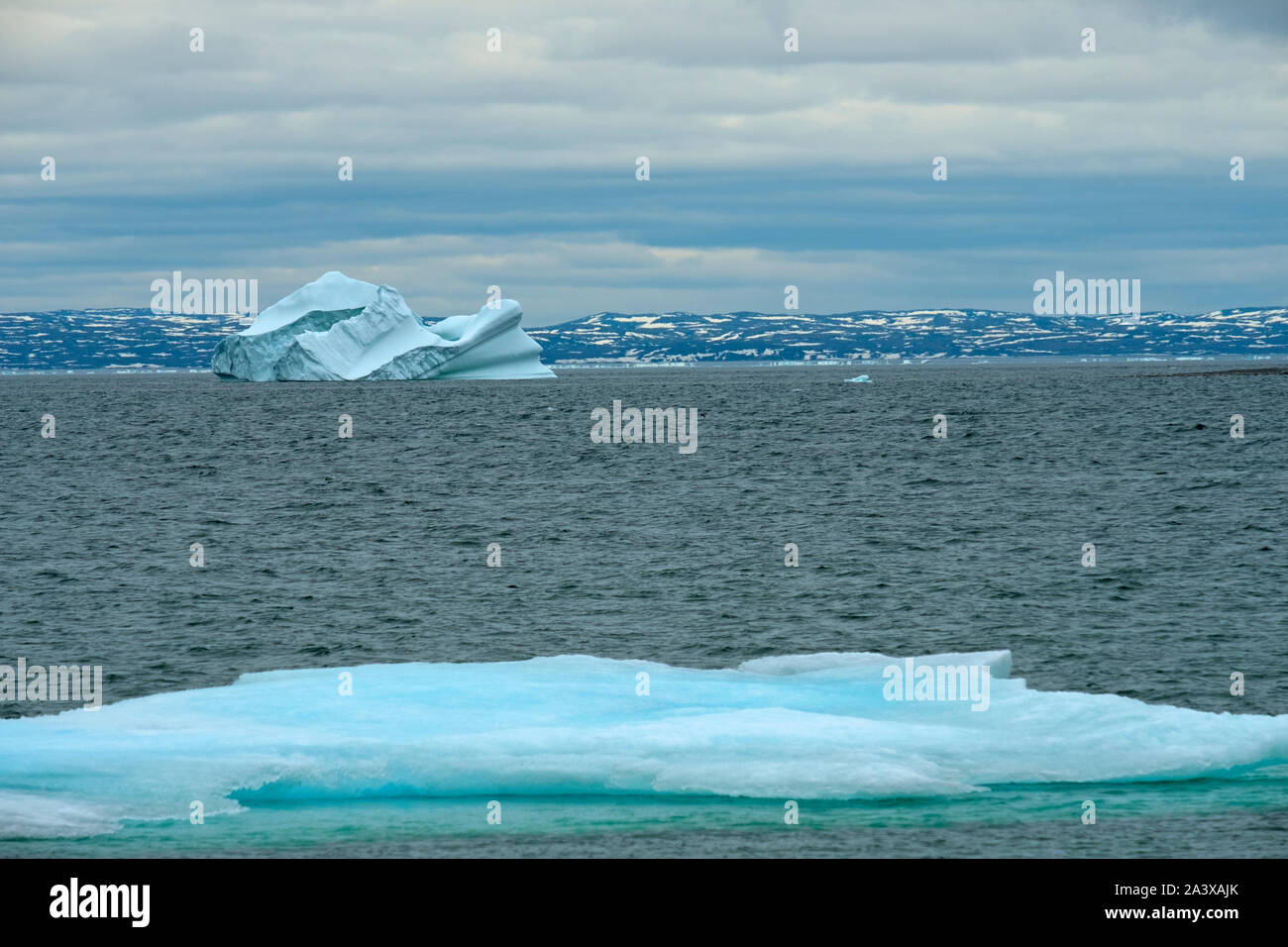 Iceberg floats near the coast at Green Island Cove, Newfoundland. Labrador coast is in the background. Stock Photo