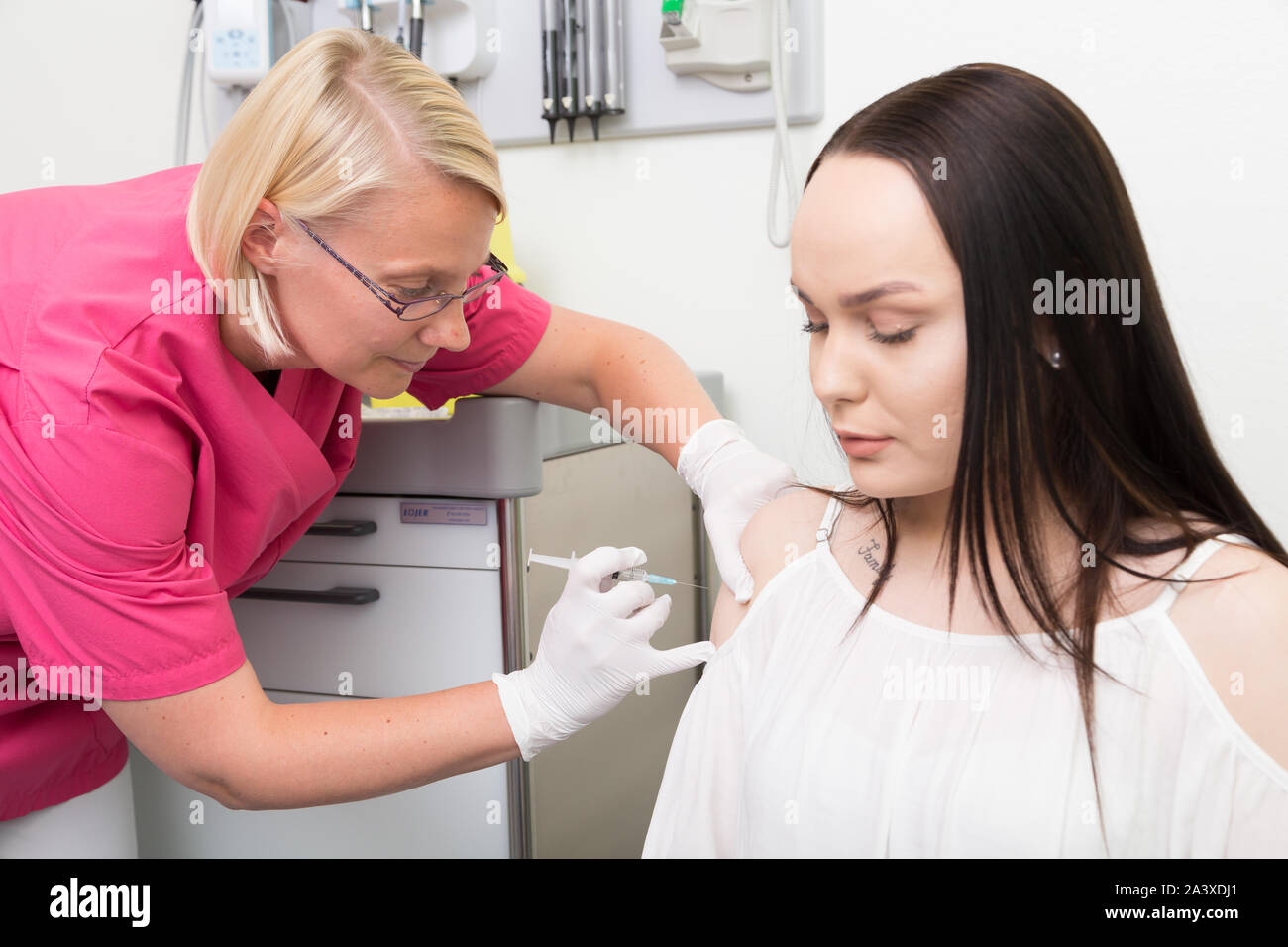 Female registered nurse giving a influenza vaccination to a young female Stock Photo