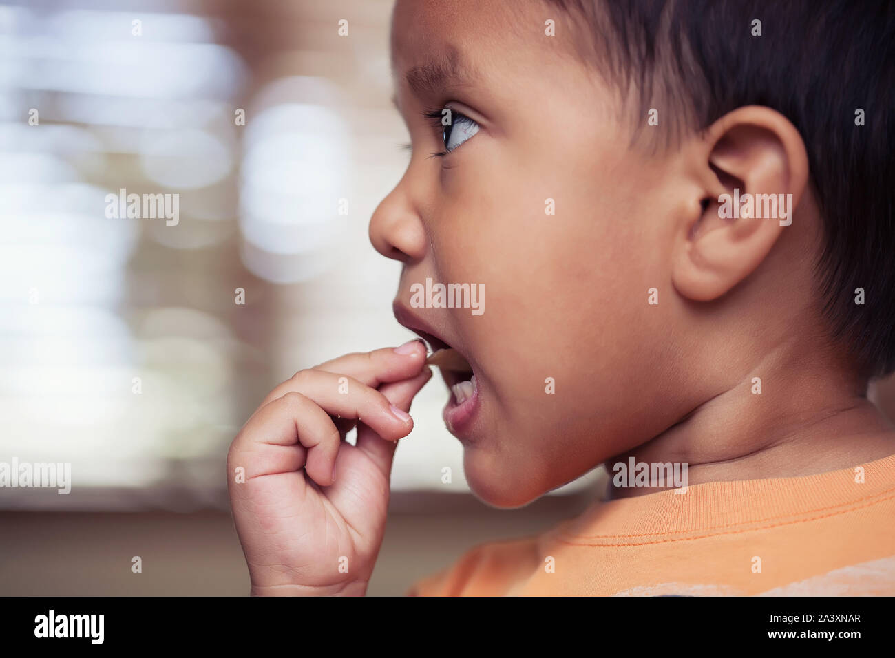 A profile view of a little kid putting a potato chip in his mouth to eat. Stock Photo