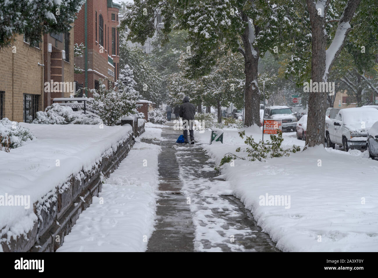 Denver, Colorado, USA- October 10, 2019: Man cleans side walk at Capitol Hill neighborhood during Denver's first snow storm of the season. Stock Photo