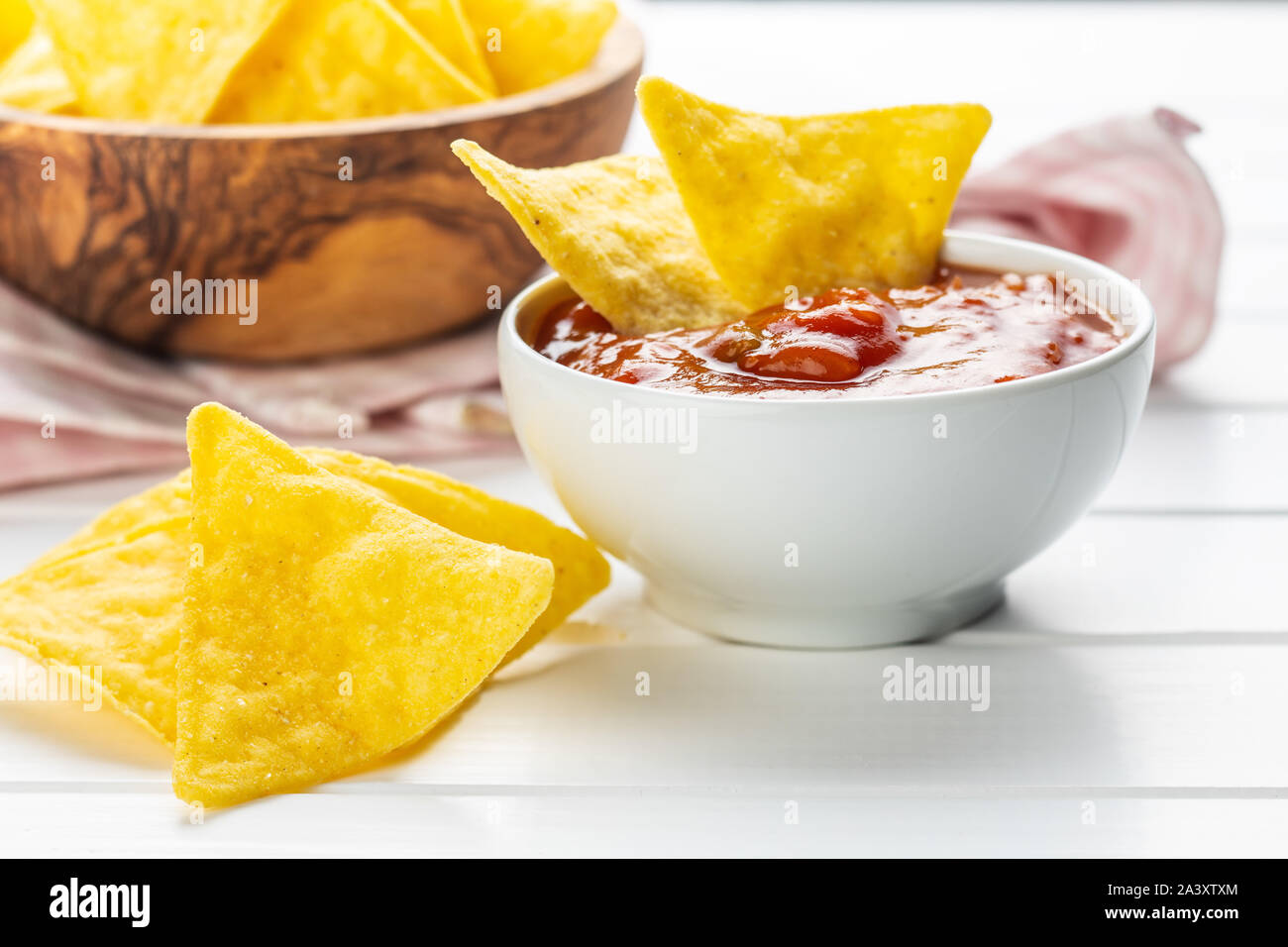 Corn nacho chips and tomato dip. Yellow tortilla chips and salsa on white table. Stock Photo